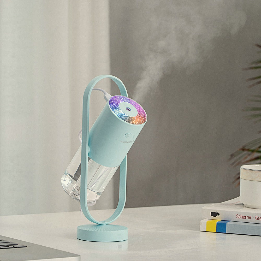 Light Blue humidifier tilted in its stand, releasing mist on a white desk beside books
